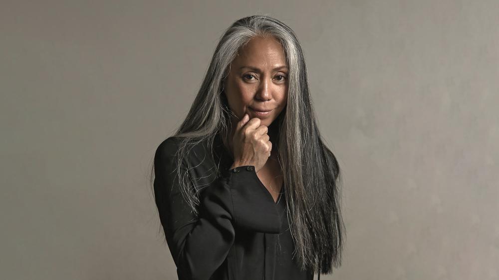 A woman stands with her hand on her chin in a blazer.