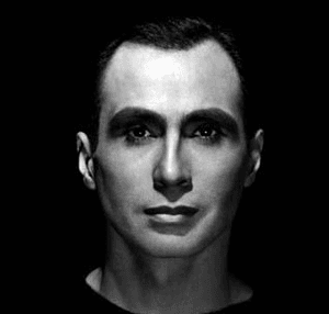 A black and white headshot of a man's face. There are dark shadows on his face.