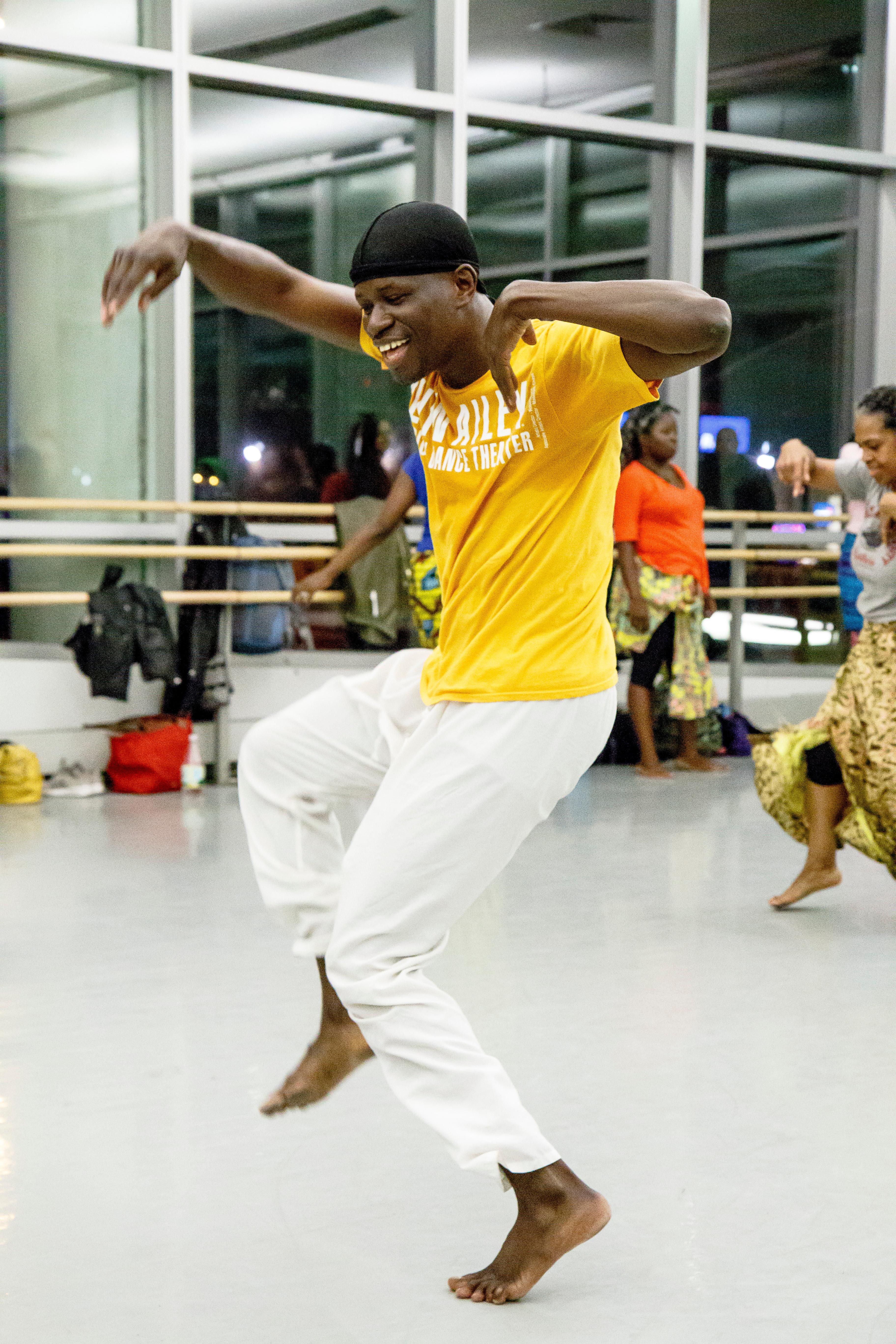 Babacar M'Baye wearing white pants and a yellow t-shirt smiling and dancing in the studio